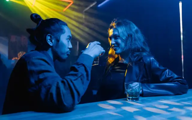 Two people talking over drinks at a neon-lit bar