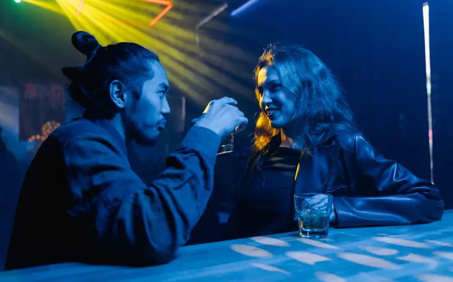 Two people talking over drinks at a neon-lit bar